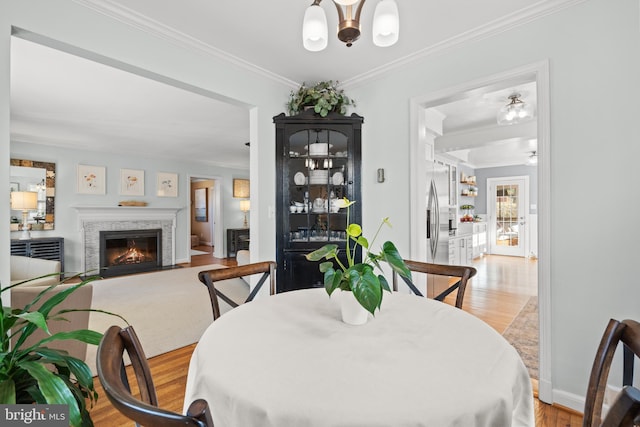 dining area with a notable chandelier, light wood-style flooring, crown molding, and a fireplace with flush hearth