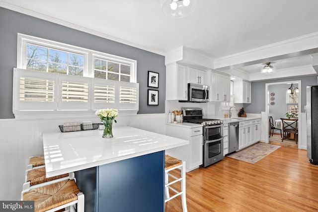 kitchen featuring a breakfast bar area, stainless steel appliances, white cabinetry, light wood-type flooring, and crown molding