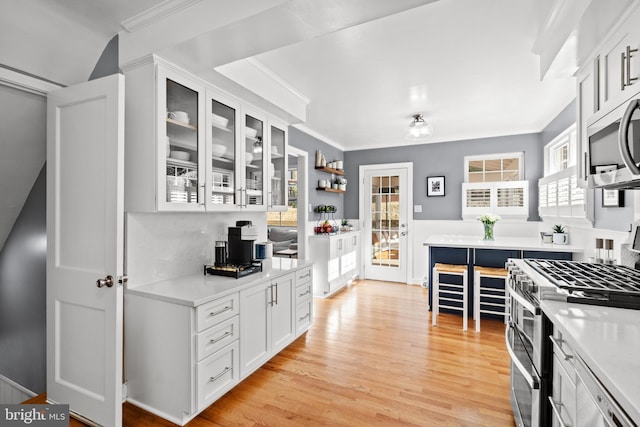 kitchen with stainless steel appliances, light wood-type flooring, light countertops, and crown molding