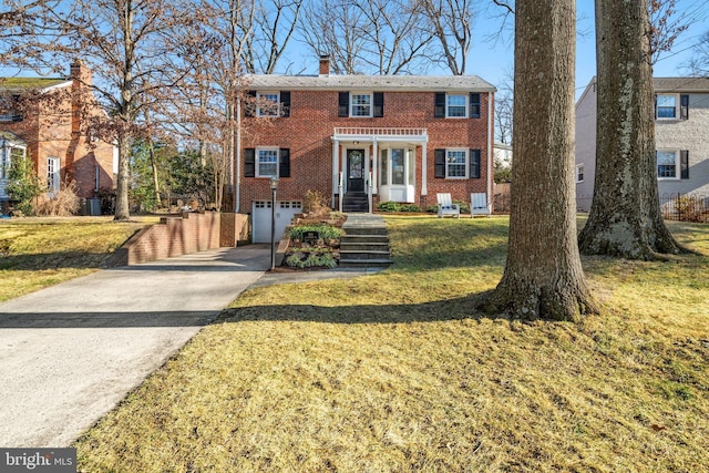 view of front of house featuring driveway, brick siding, a chimney, an attached garage, and a front yard