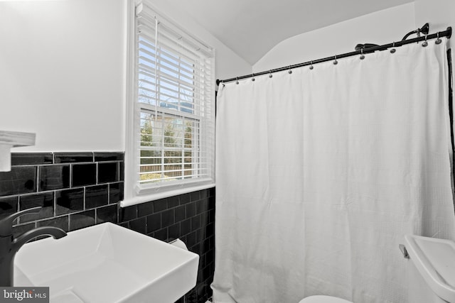 bathroom with a shower with shower curtain, a sink, tile walls, vaulted ceiling, and wainscoting