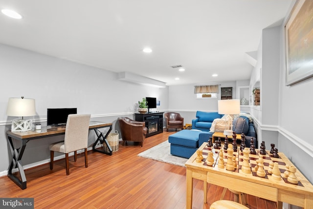 interior space featuring a glass covered fireplace, visible vents, recessed lighting, and wood finished floors