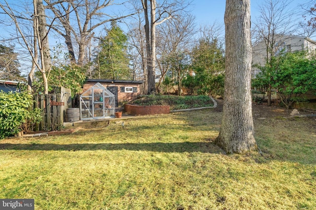 view of yard featuring an outdoor structure, a greenhouse, fence, and a garden