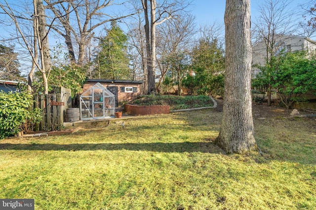 view of yard with a greenhouse, fence, a vegetable garden, and an outdoor structure