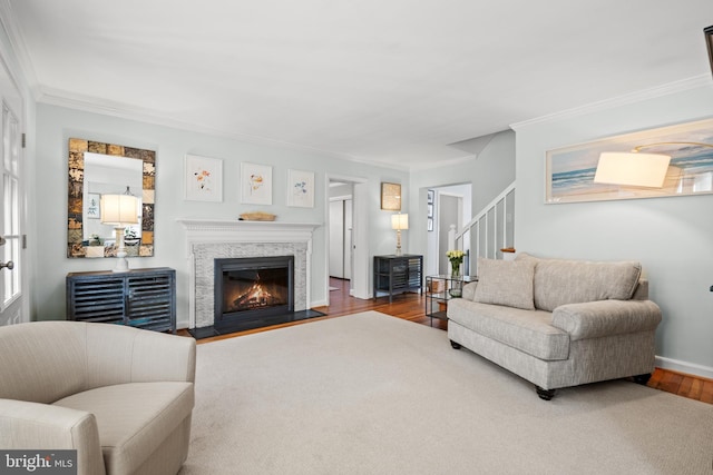 living area with baseboards, stairway, wood finished floors, a lit fireplace, and crown molding