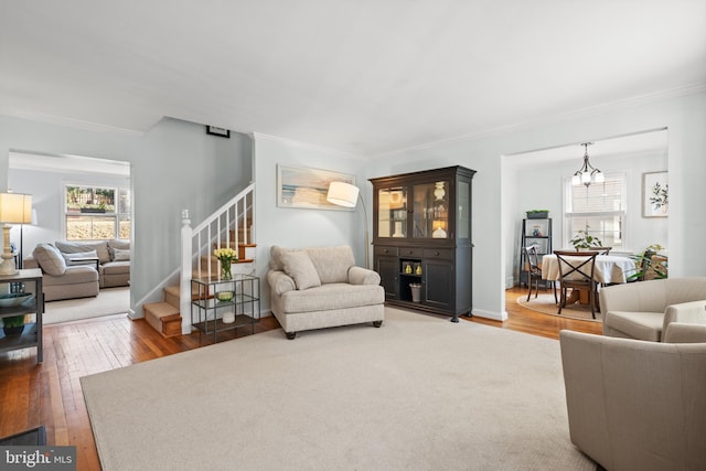 living area with ornamental molding, a notable chandelier, stairway, and hardwood / wood-style floors