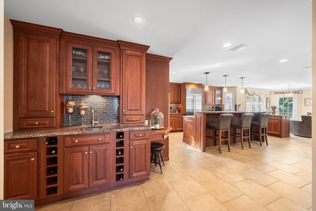 bar featuring tasteful backsplash, stainless steel built in fridge, light tile patterned floors, hanging light fixtures, and a sink