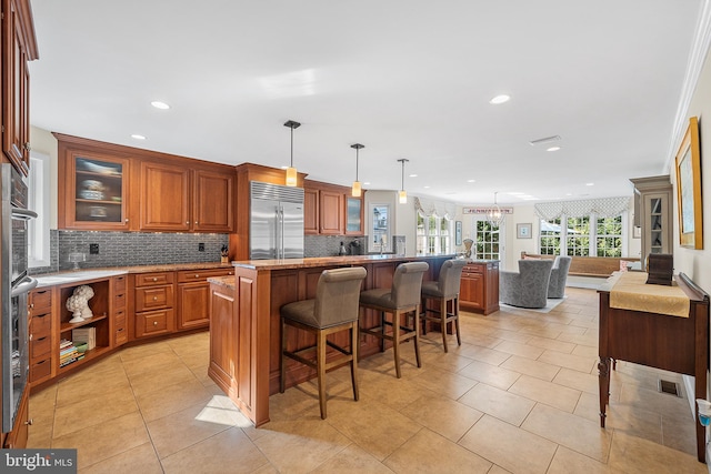 kitchen with a breakfast bar area, tasteful backsplash, stainless steel built in refrigerator, and brown cabinetry