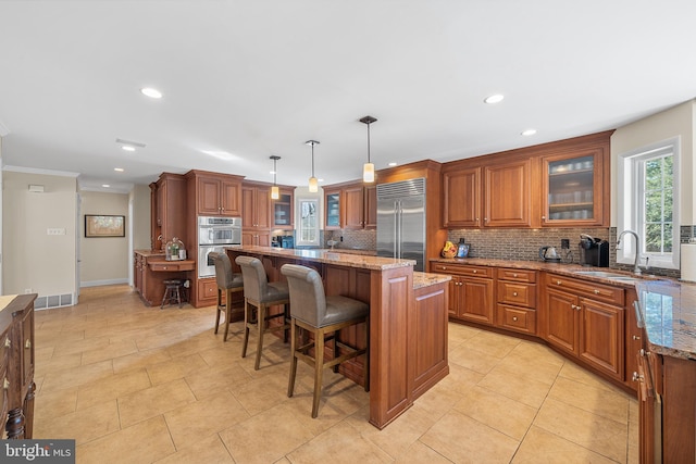 kitchen with brown cabinetry, backsplash, stainless steel appliances, and a sink