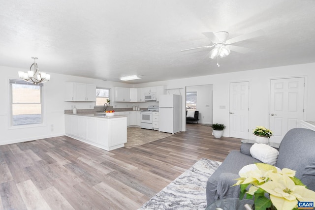 kitchen featuring white appliances, light wood finished floors, open floor plan, a peninsula, and a sink