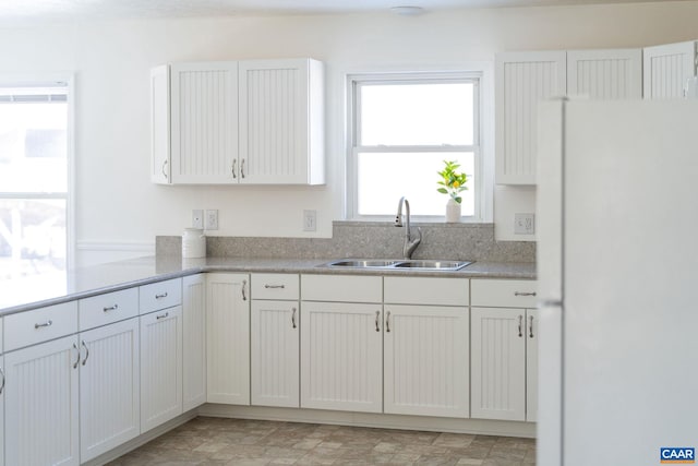 kitchen featuring light countertops, a sink, freestanding refrigerator, and white cabinetry