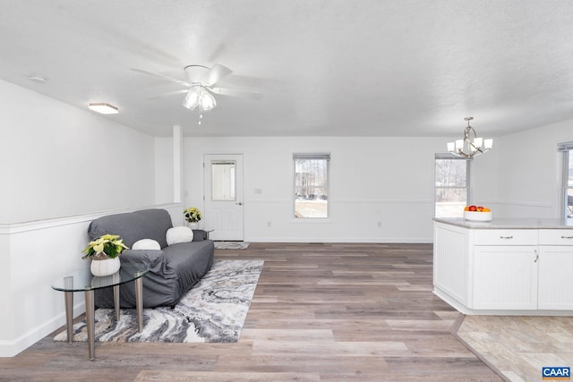 sitting room featuring baseboards, light wood finished floors, and ceiling fan with notable chandelier