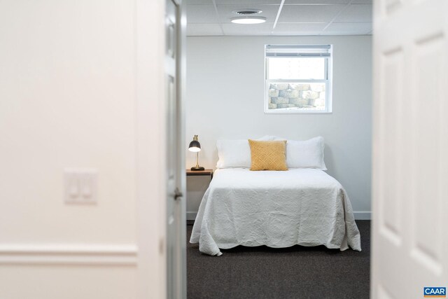 carpeted bedroom featuring a drop ceiling and baseboards