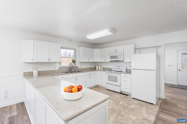 kitchen with a peninsula, white appliances, a sink, white cabinets, and light countertops