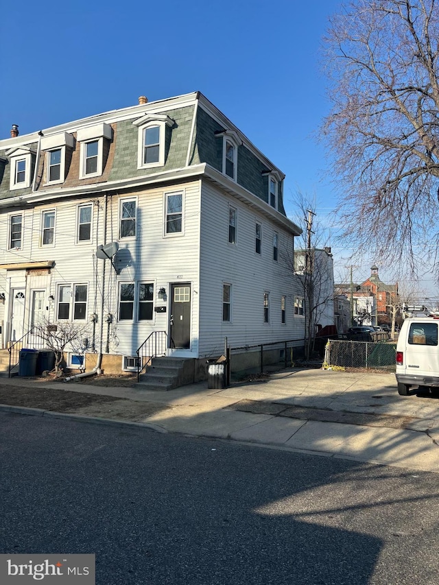 view of front facade featuring cooling unit, roof with shingles, fence, and mansard roof