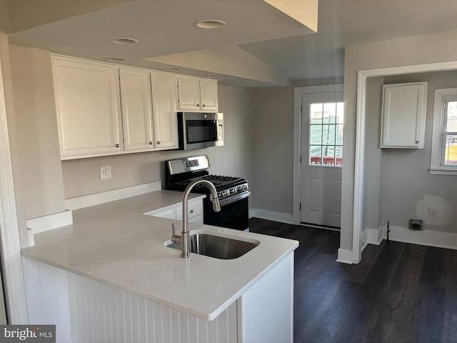 kitchen with dark wood-style flooring, stainless steel appliances, white cabinets, a sink, and a peninsula