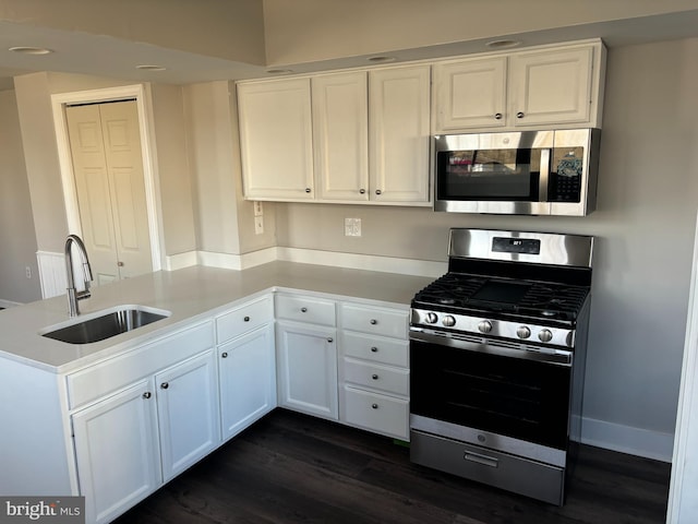 kitchen featuring a peninsula, dark wood-style flooring, a sink, white cabinetry, and appliances with stainless steel finishes