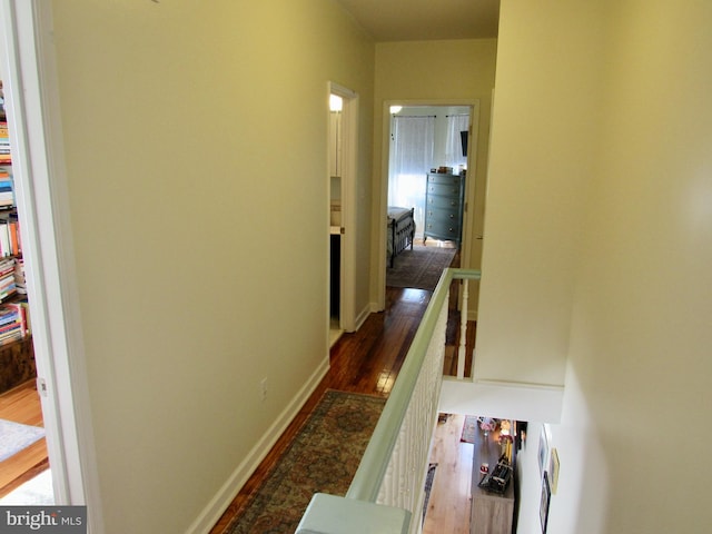 hall with dark wood-style floors, baseboards, and an upstairs landing