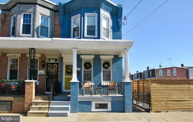 view of property with a porch, fence, and brick siding