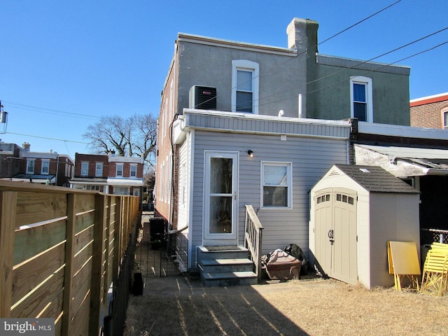 back of property with a storage unit, central AC unit, entry steps, fence, and an outdoor structure