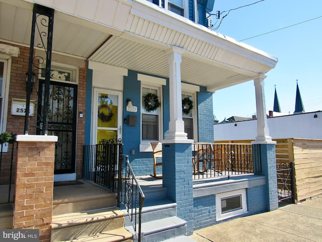 doorway to property featuring a porch and brick siding