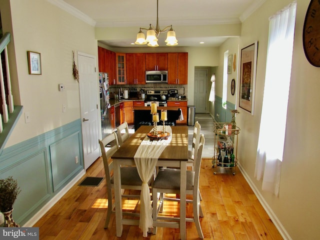 dining area with ornamental molding, wainscoting, a notable chandelier, and light wood-style flooring