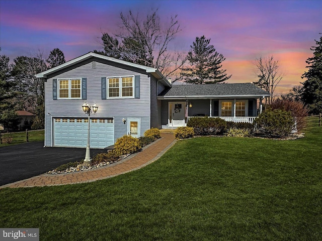 split level home featuring a garage, a porch, aphalt driveway, and a lawn