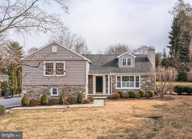 view of front facade with stone siding, a chimney, a front yard, and fence