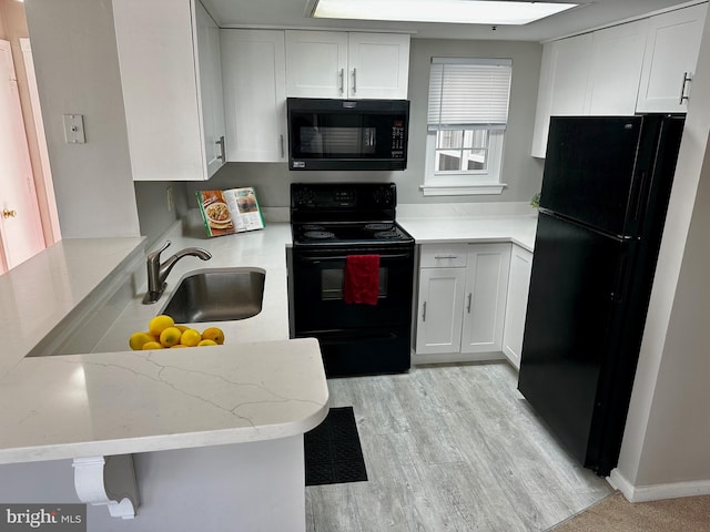 kitchen featuring white cabinets, light wood-style floors, light stone counters, black appliances, and a sink