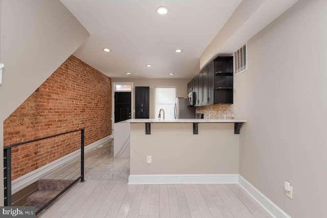 kitchen featuring brick wall, a kitchen breakfast bar, a peninsula, stainless steel appliances, and open shelves