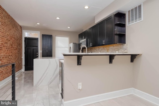 kitchen with a breakfast bar, open shelves, visible vents, appliances with stainless steel finishes, and brick wall