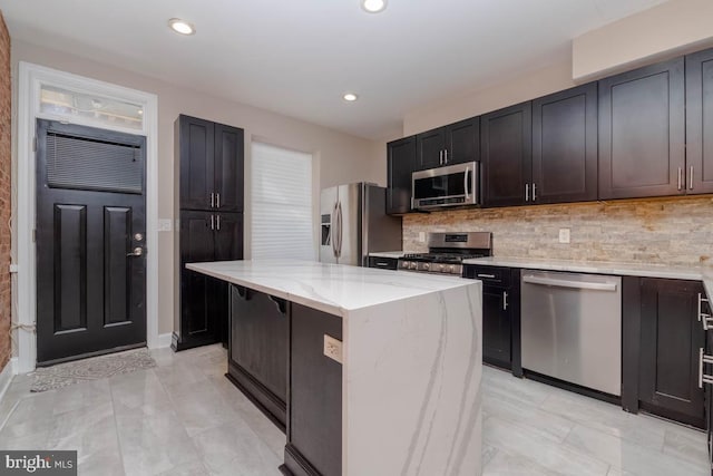 kitchen with light stone counters, a center island, recessed lighting, backsplash, and appliances with stainless steel finishes