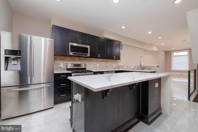 kitchen with light stone counters, stainless steel appliances, decorative backsplash, a kitchen island, and a kitchen breakfast bar