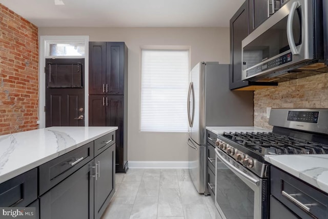 kitchen with appliances with stainless steel finishes, brick wall, light stone counters, and tasteful backsplash