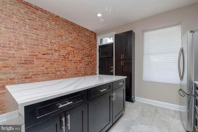 kitchen with brick wall, baseboards, light stone counters, and freestanding refrigerator