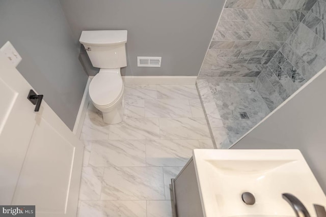 bathroom featuring marble finish floor, visible vents, toilet, tiled shower, and baseboards