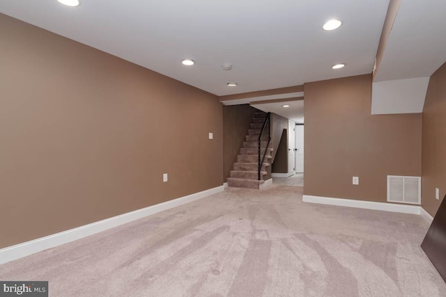 finished basement featuring baseboards, stairs, visible vents, and light colored carpet