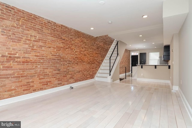 unfurnished room with recessed lighting, brick wall, baseboards, light wood-style floors, and stairway