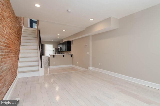 unfurnished living room with recessed lighting, brick wall, baseboards, light wood-style floors, and stairway