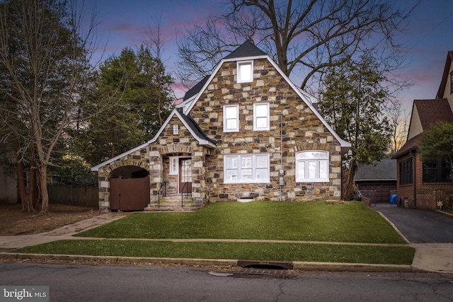 tudor house featuring stone siding, fence, and a yard