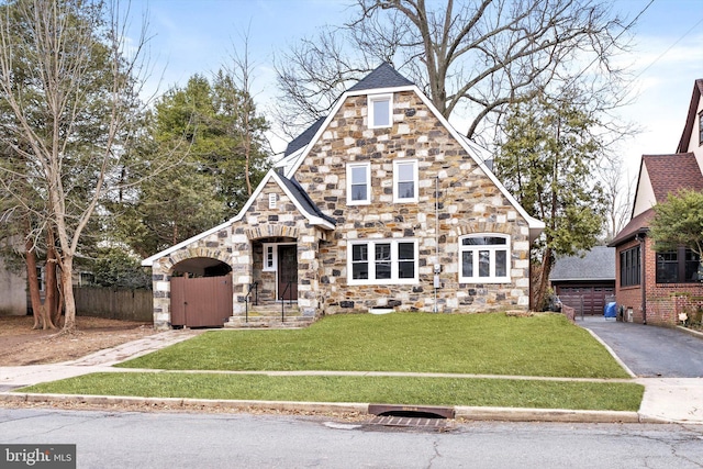 view of front of house with a garage, stone siding, fence, and a front yard