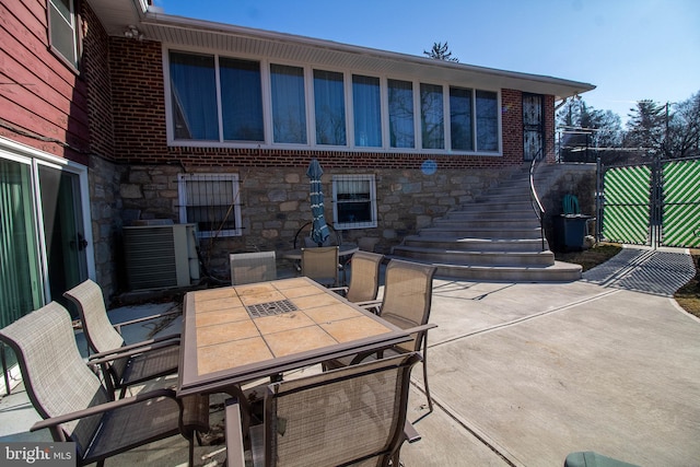 view of patio with central AC, outdoor dining area, stairway, and fence