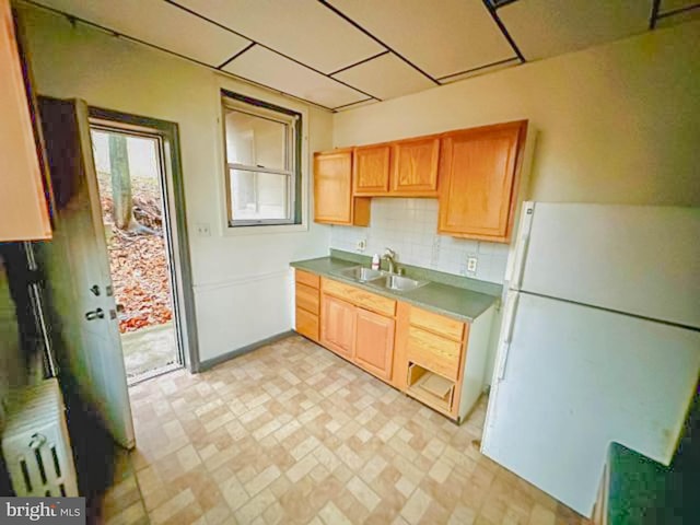 kitchen featuring freestanding refrigerator, a sink, and backsplash