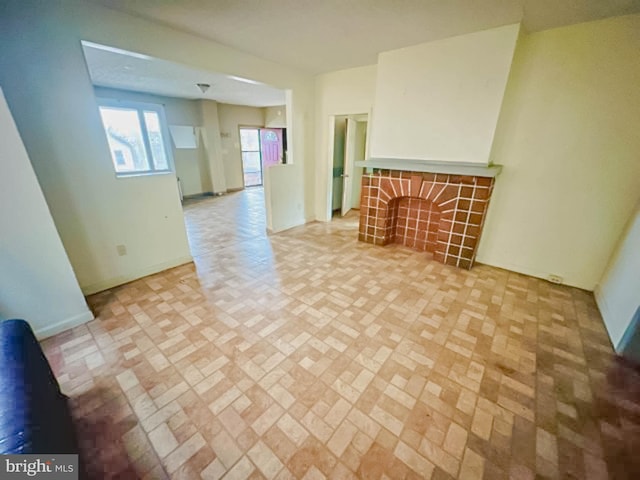 unfurnished living room with baseboards, a fireplace, and brick patterned floor