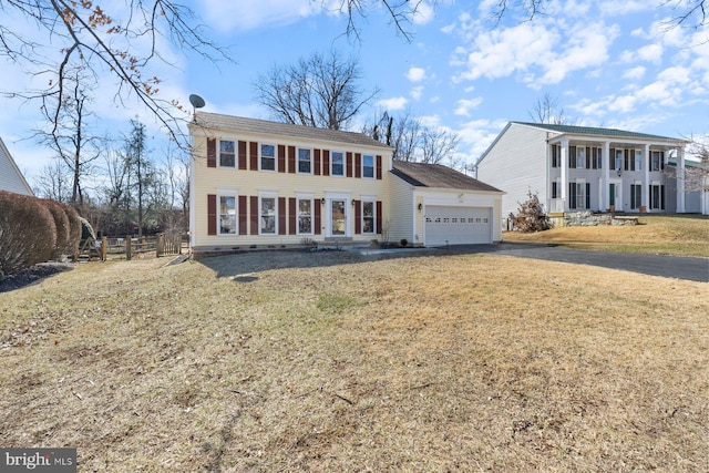 colonial-style house featuring a garage, aphalt driveway, a front yard, and fence