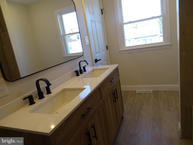 bathroom with double vanity, wood finished floors, a sink, and baseboards