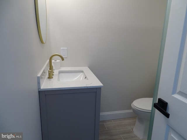 half bathroom with wood finish floors, baseboards, vanity, and toilet