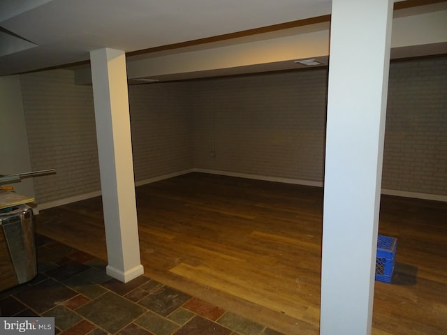 finished basement with brick wall, dark wood-type flooring, and baseboards