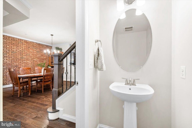 bathroom with visible vents, ornamental molding, brick wall, wood finished floors, and a chandelier