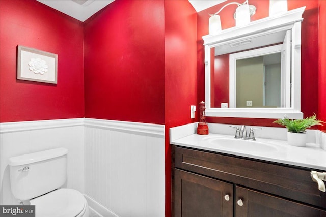 bathroom with toilet, vanity, and wainscoting